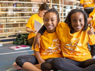 Two Girls on the Run participants in yellow shirts run while smiling at the camera